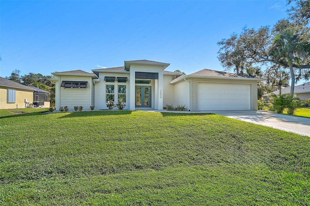 A single-story house with a white stucco exterior, a two-car garage, and a front lawn — 2690 PEBBLE CREEK PLACE, PORT CHARLOTTE, FL