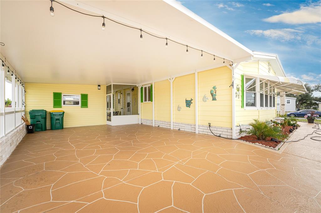 A yellow mobile home features a large covered carport with a patterned concrete floor — 6290 GREENFINCH ROAD, ENGLEWOOD, FL