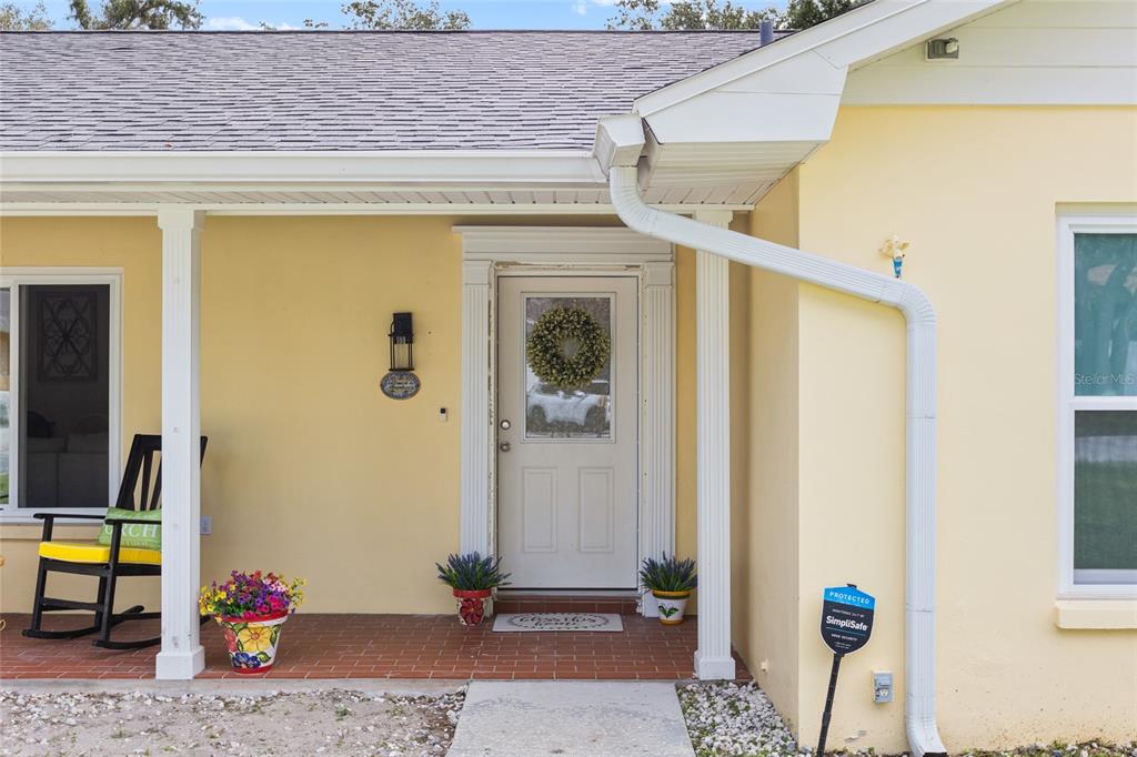 The exterior of a yellow house features a front door, a porch, and a rocking chair — 1103 RIDGEFIELD DRIVE, VALRICO, FL