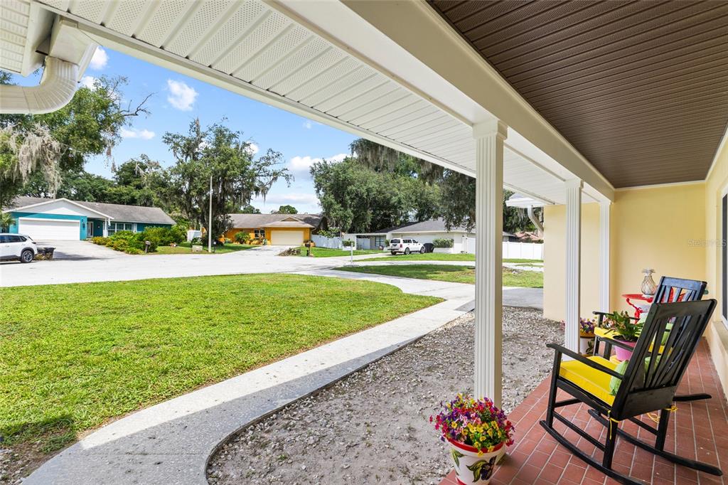 A covered front porch with rocking chairs overlooks a suburban street and front yard — 1103 RIDGEFIELD DRIVE, VALRICO, FL
