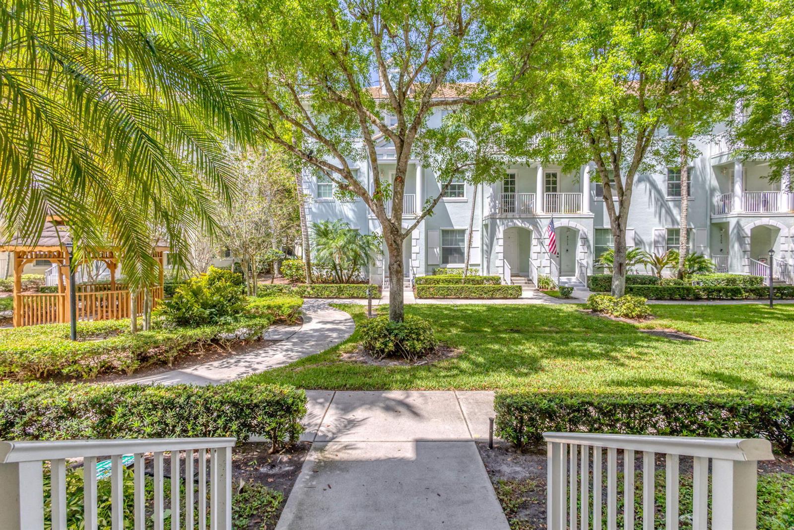 A multi-story residential building with balconies stands behind a landscaped lawn and paved walkway — 4320 Blowing Point Place, Jupiter FL 33458, JUPITER, FL