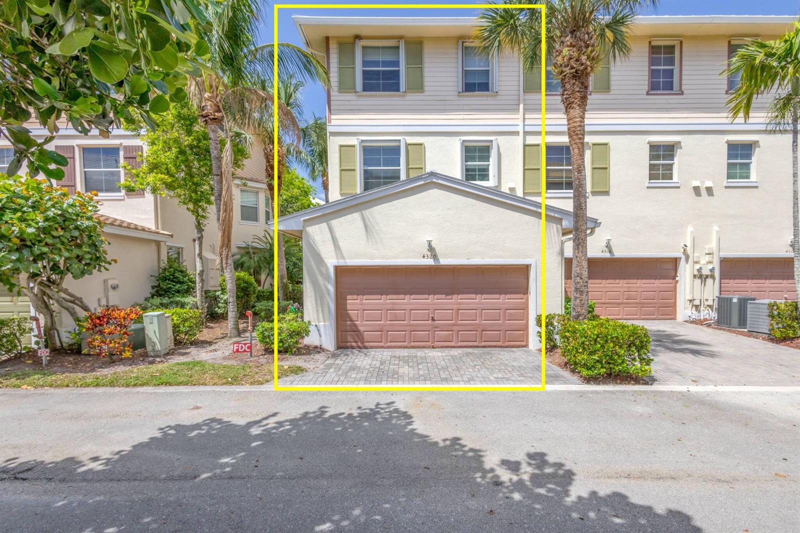 A three-story townhouse with a beige exterior, green shutters, and a two-car garage — 4320 Blowing Point Place, Jupiter FL 33458, JUPITER, FL