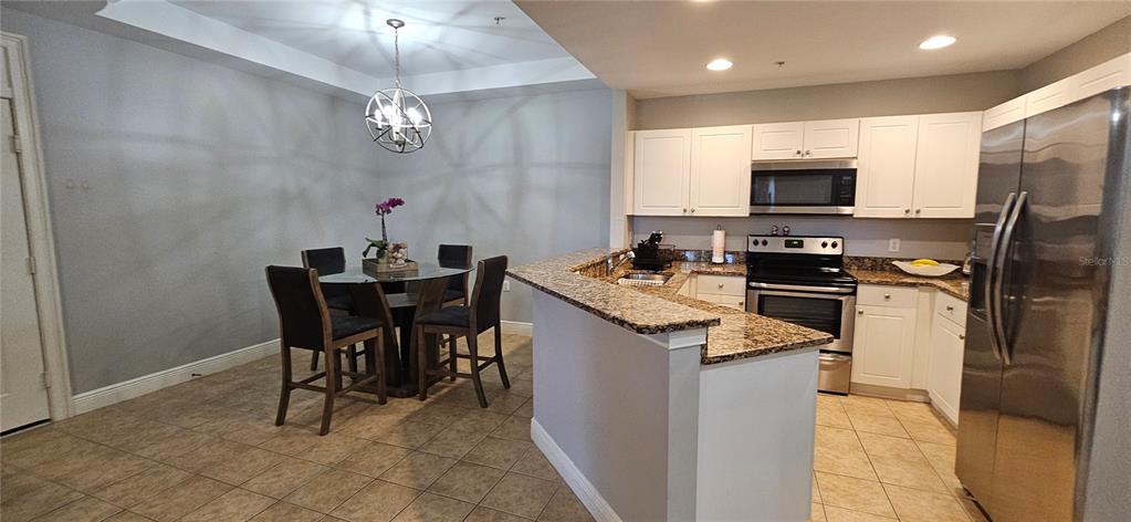 A kitchen with white cabinets and granite countertops opens to a dining area with seating — 1502 SW 50TH STREET UNIT 104, CAPE CORAL, FL