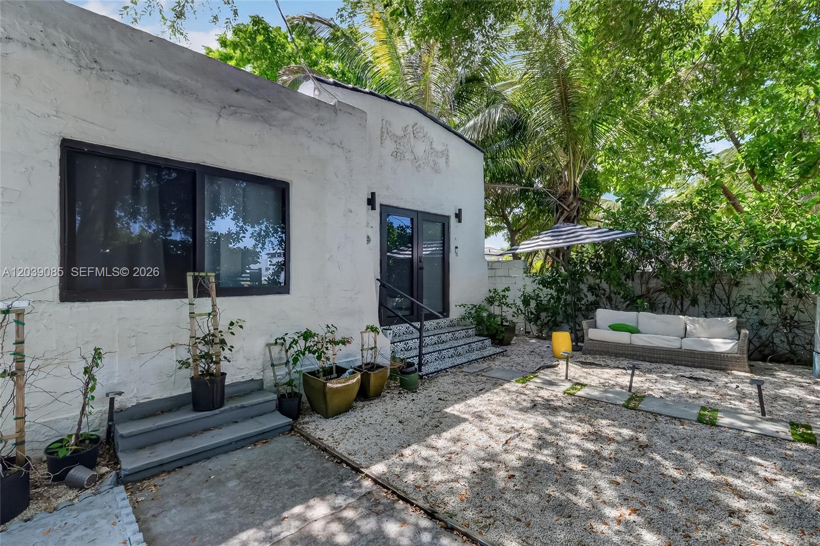 A white stucco house exterior features a gravel patio, potted plants, and outdoor seating — 8280 NE 1st Pl, Miami FL 33138, MIAMI, FL