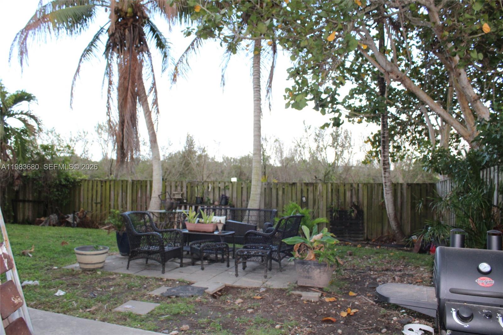 A backyard patio features black wicker furniture, potted plants, and a grill near a fence — 9818 SW 222nd Ter, Cutler Bay FL 33190, CUTLER BAY, FL