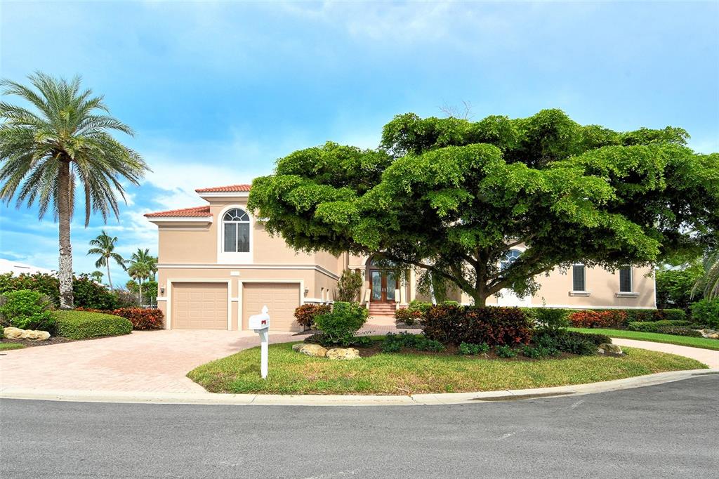 A two-story tan house with a large tree, a palm tree, and a paved driveway — 591 PUTTING GREEN LANE, LONGBOAT KEY, FL