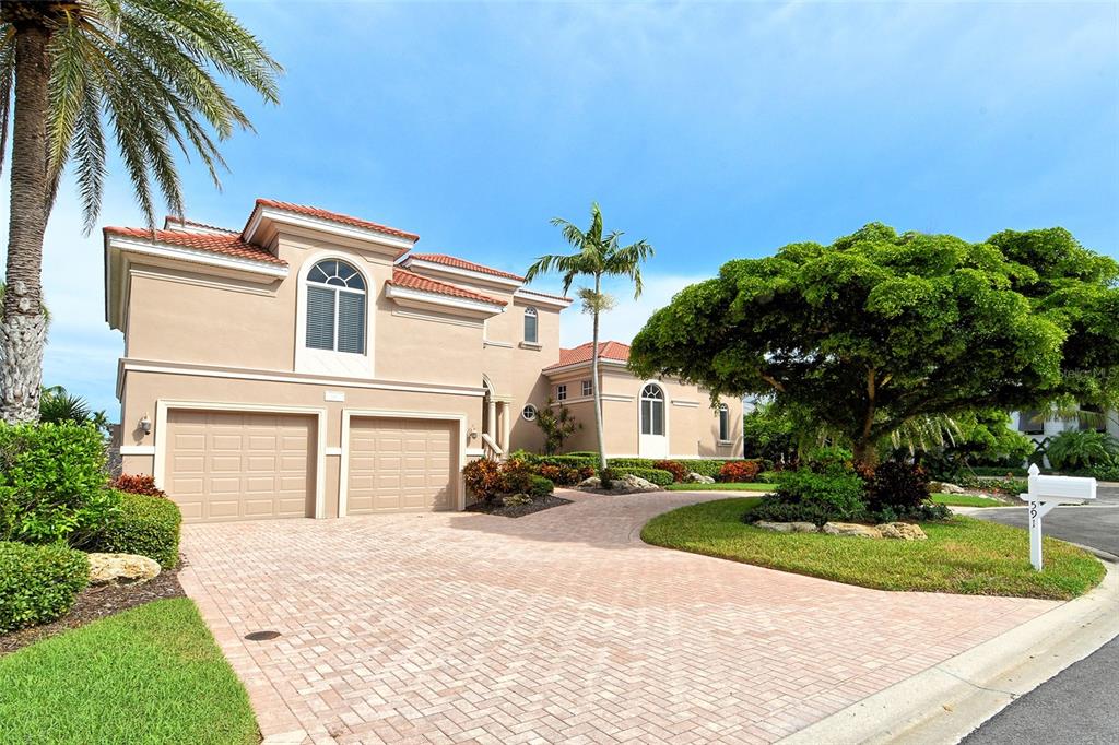 A two-story house with a beige stucco exterior, a paver driveway, and a large tree — 591 PUTTING GREEN LANE, LONGBOAT KEY, FL