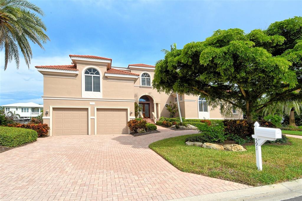 A two-story tan house with a paved driveway, two-car garage, and a large front tree — 591 PUTTING GREEN LANE, LONGBOAT KEY, FL