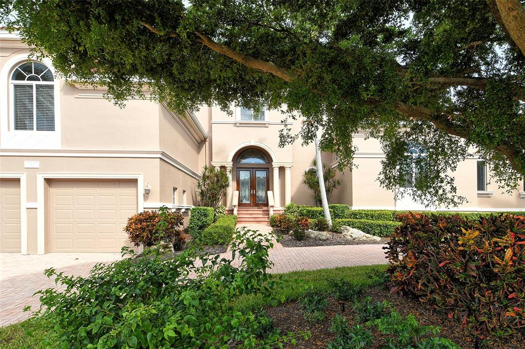 A two-story beige house with a brick driveway, arched entryway, and a large front tree — 591 PUTTING GREEN LANE, LONGBOAT KEY, FL