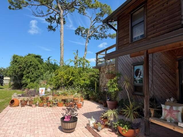 A brick patio features numerous potted plants and a wooden porch swing beside a house — 9219 Nickels, Boynton Beach FL 33436, BOYNTON BEACH, FL