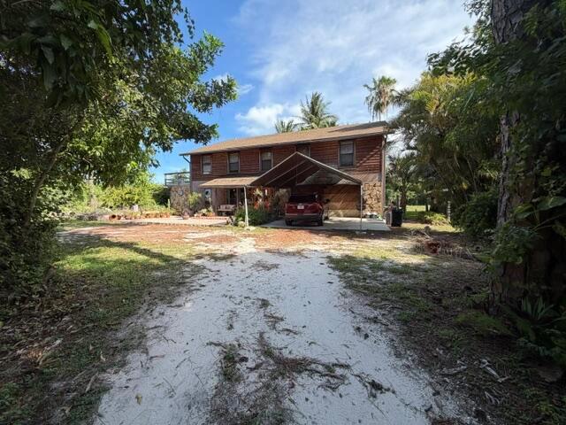 A two-story house with a wooden exterior and a metal carport sits on a sandy lot — 9219 Nickels, Boynton Beach FL 33436, BOYNTON BEACH, FL