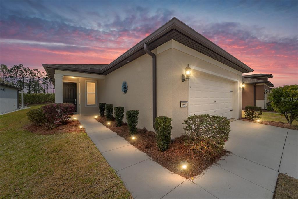 A single-story house exterior features a garage, a walkway with landscape lighting, and a sunset — 5882 SW 93RD CIRCLE, OCALA, FL