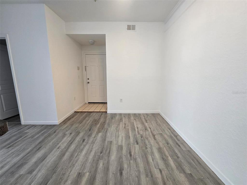 A room with light gray wood-look flooring and white walls leads to an entryway door — 17108 CARRINGTON PARK DRIVE UNIT 707, TAMPA, FL