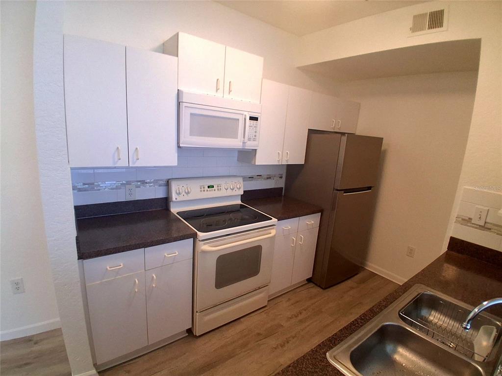 A kitchen features white cabinets, dark countertops, a white stove, and a stainless steel refrigerator — 17108 CARRINGTON PARK DRIVE UNIT 707, TAMPA, FL