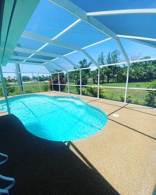 A screened-in swimming pool with a textured patio deck overlooks a grassy yard and trees — 295 ANNAPOLIS LANE, ROTONDA WEST, FL