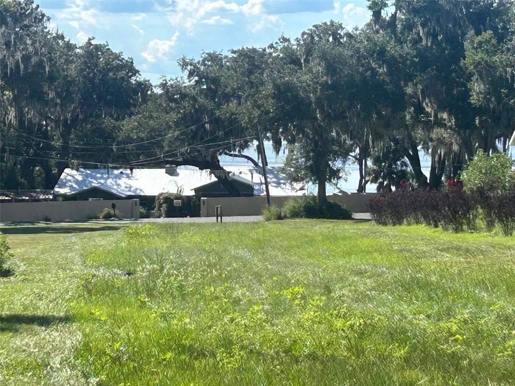 A grassy lot overlooks a house with a white roof and mature trees — 15365 SE 140TH AVENUE ROAD, WEIRSDALE, FL