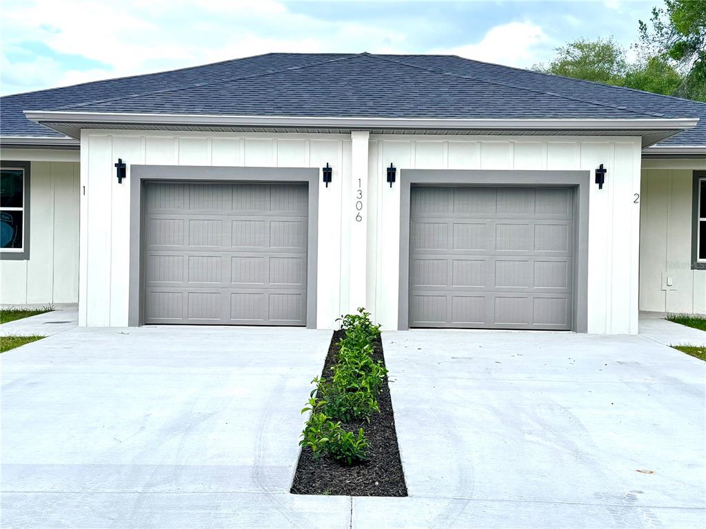 A duplex exterior features two gray garage doors, white vertical siding, and a central planter — 1306 NW 8TH STREET UNIT 1 & 2, OCALA, FL