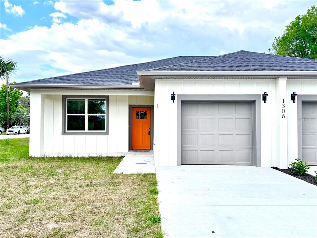A single-story house exterior features white board-and-batten siding, a gray garage door, and an orange door — 1306 NW 8TH STREET UNIT 1 & 2, OCALA, FL