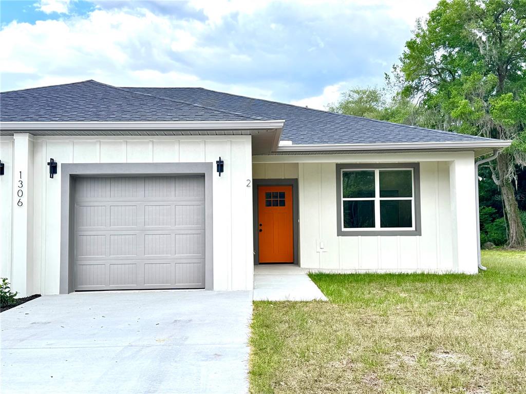 A single-story house features white vertical siding, a gray garage door, and an orange front door — 1306 NW 8TH STREET UNIT 1 & 2, OCALA, FL