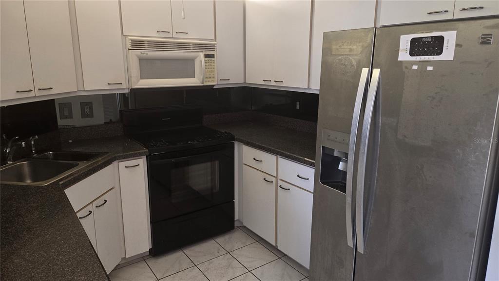 A kitchen features white cabinets, dark countertops, a black stove, and a stainless steel refrigerator — 213 RUBENS DRIVE UNIT H, NOKOMIS, FL