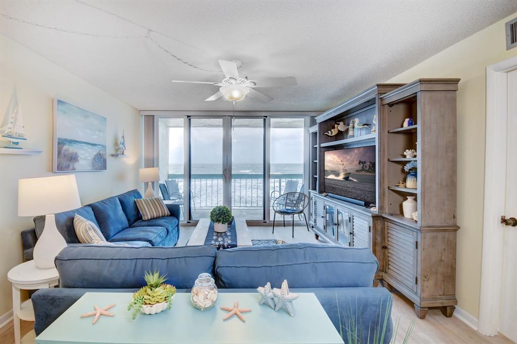 A living room with blue sofas, a large entertainment center, and a balcony overlooking the ocean — 9940 S Ocean Drive # 505, Jensen Beach FL 34957, JENSEN BEACH, FL