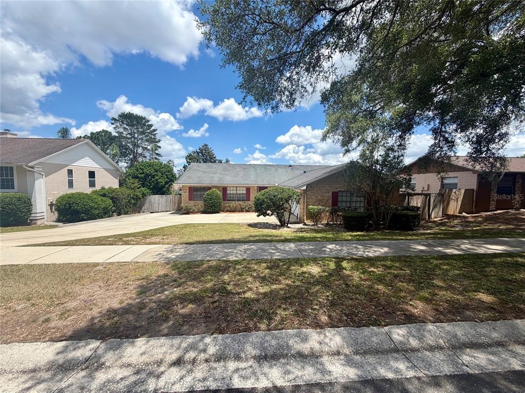 A single-story brick house with a large driveway and lawn under a blue sky — 37 HOLLOW BRANCH ROAD, APOPKA, FL