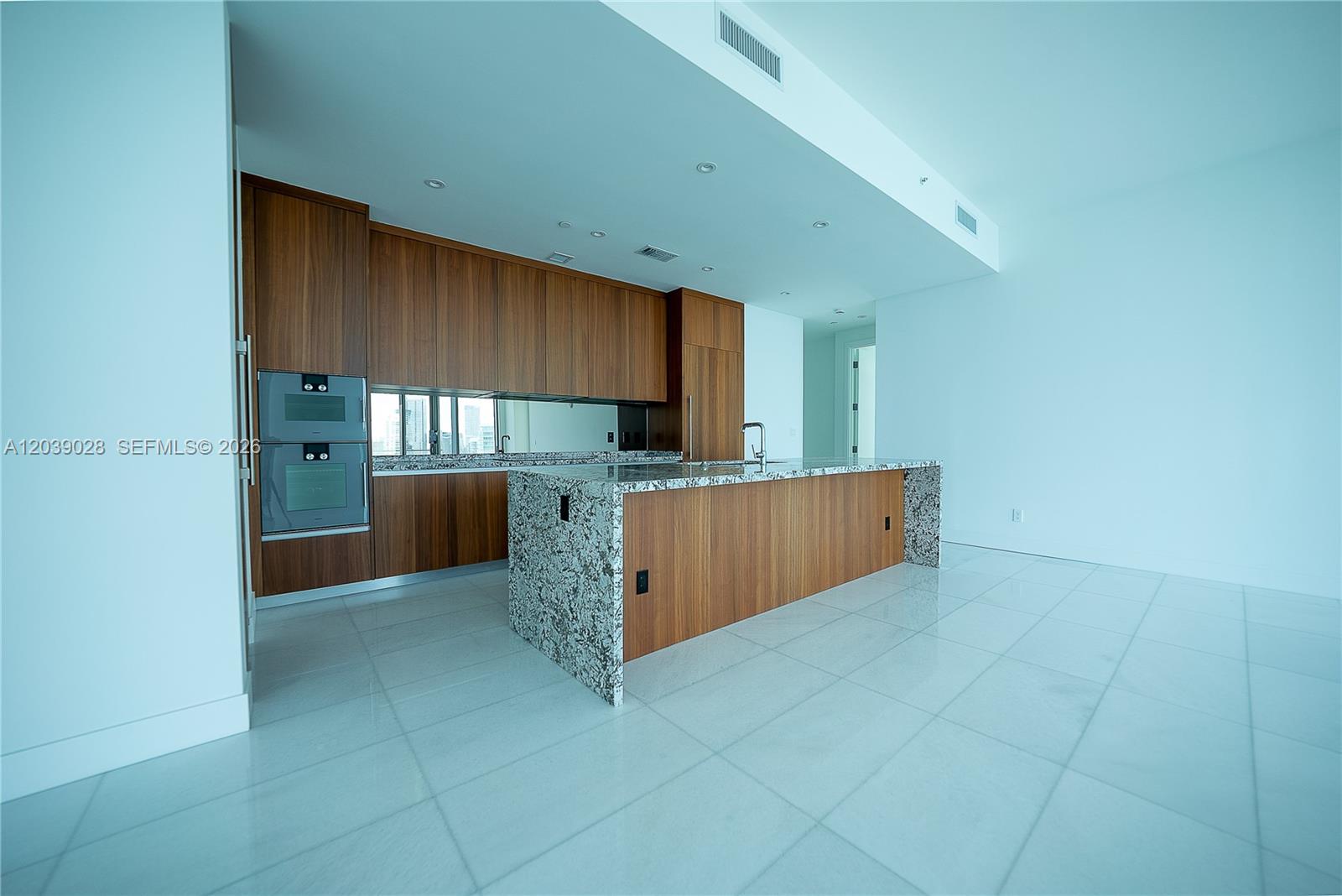 A modern kitchen features wood cabinetry, granite countertops, a large island, and white tile flooring — 175 SE 25th Rd # 2704, Miami FL 33129, MIAMI, FL