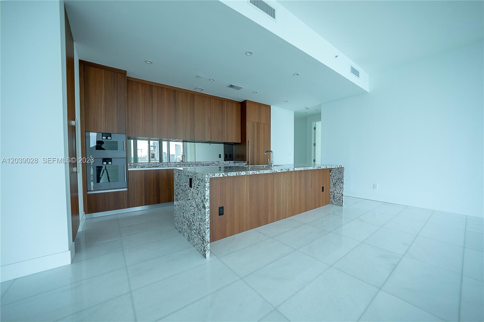 A modern kitchen features wood cabinetry, granite countertops, a central island, and white tile flooring — 175 SE 25th Rd # 2704, Miami FL 33129, MIAMI, FL