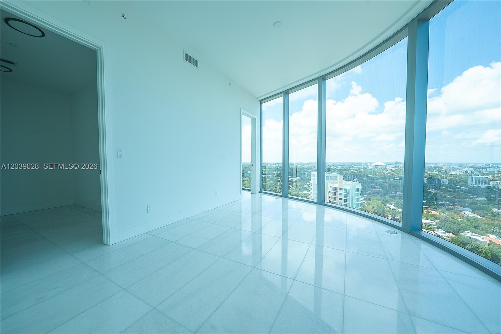 An empty room with white tile floors and floor-to-ceiling windows overlooking a city landscape — 175 SE 25th Rd # 2704, Miami FL 33129, MIAMI, FL
