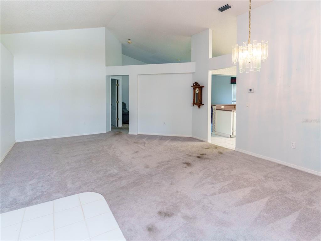 A spacious living room features vaulted ceilings, gray carpeting, and a crystal chandelier — 7207 SHARPSBURG BOULEVARD, NEW PORT RICHEY, FL