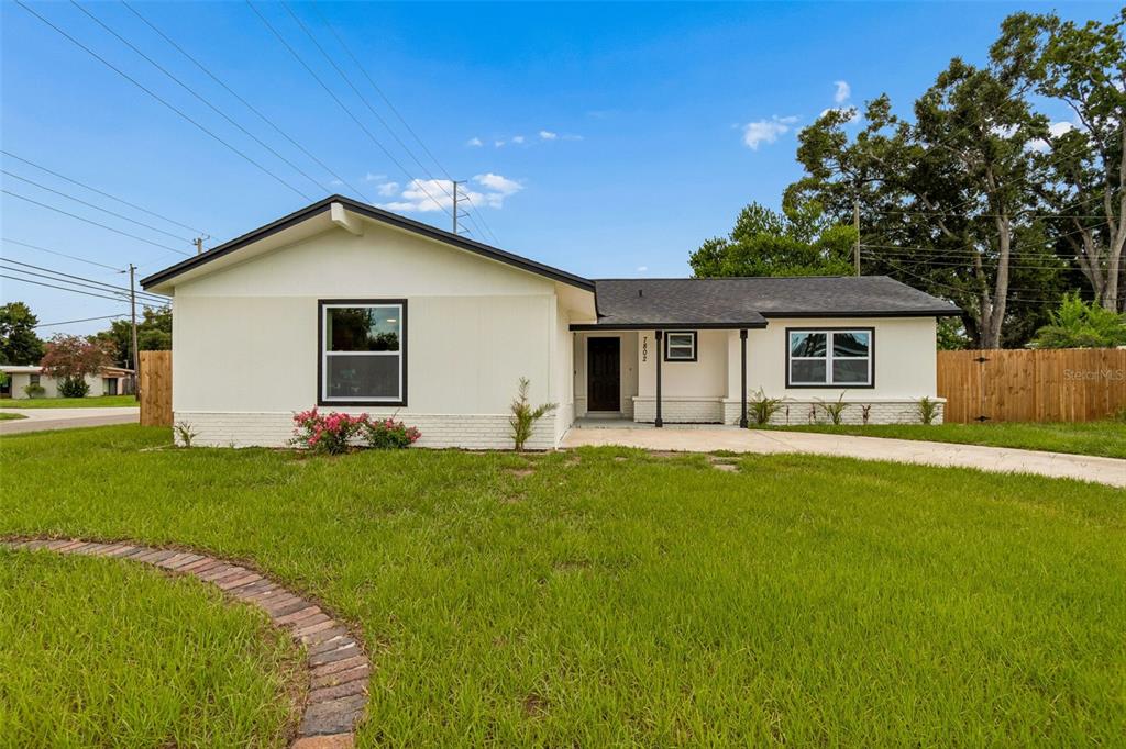 A single-story house with white siding, a dark roof, and a brick walkway on grass — 7802 N MATANZAS AVENUE, TAMPA, FL