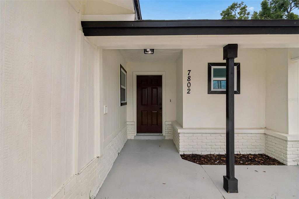 A covered entryway features a brown front door, white brick accents, and a black post — 7802 N MATANZAS AVENUE, TAMPA, FL