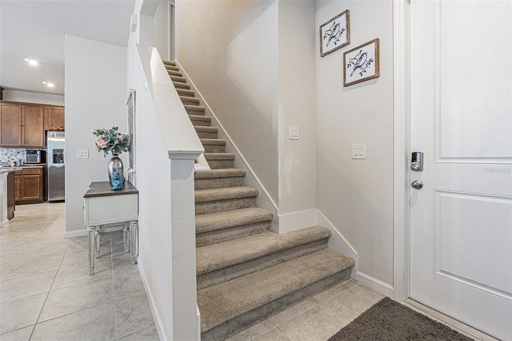 A carpeted staircase leads to an upper floor next to a white front door — 11904 THORNCREST DRIVE, SPRING HILL, FL