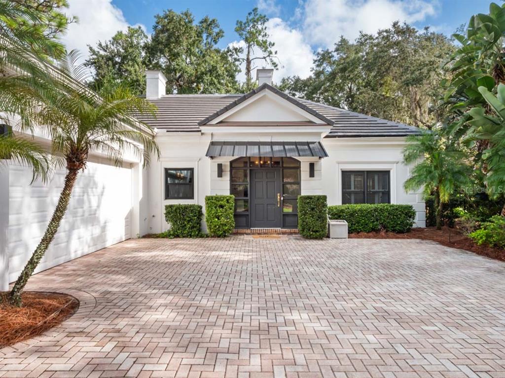 A white house with a dark roof and front door features a brick paver driveway — 10457 CROMWELL GROVE TERRACE, ORLANDO, FL
