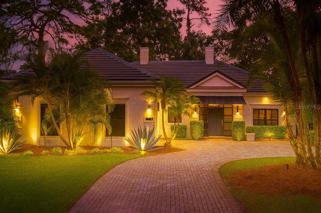 A single-story house with a paved driveway, palm trees, and warm exterior lighting at dusk — 10457 CROMWELL GROVE TERRACE, ORLANDO, FL