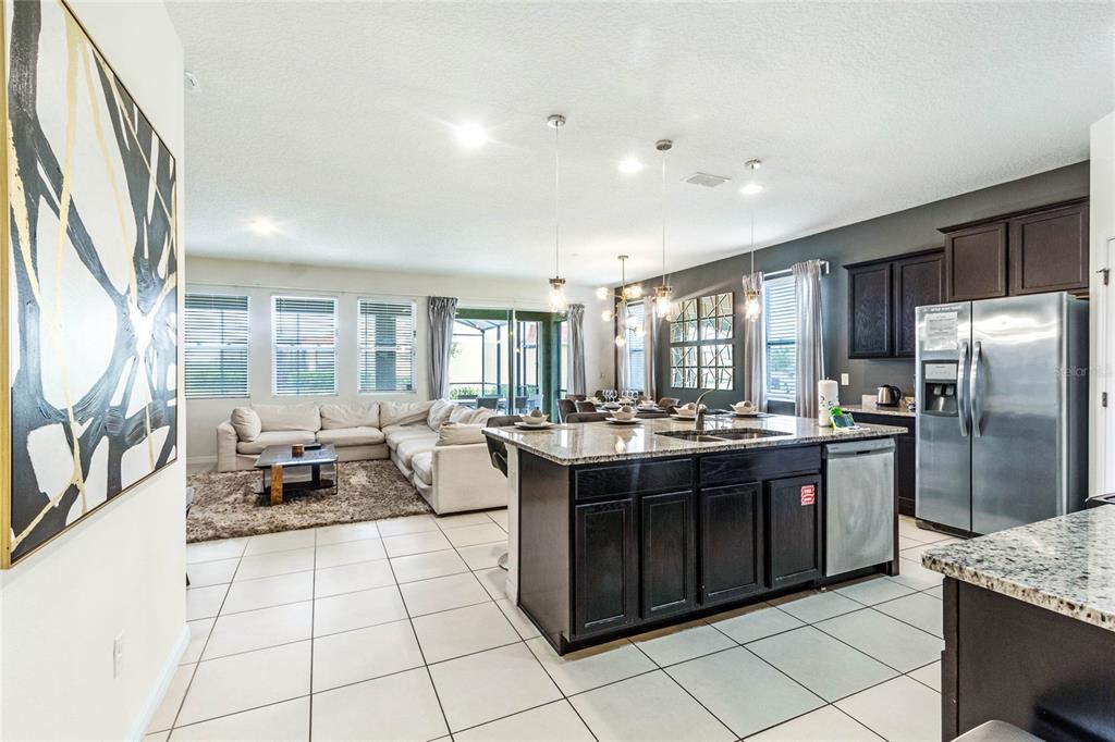 An open-concept kitchen with dark cabinets and granite countertops overlooks a living room area — 6070 BROAD OAK DRIVE, DAVENPORT, FL