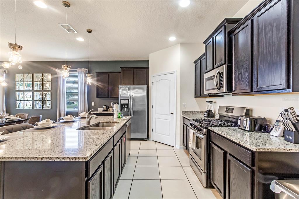 A kitchen features dark wood cabinets, granite countertops, stainless steel appliances, and a large island — 6070 BROAD OAK DRIVE, DAVENPORT, FL