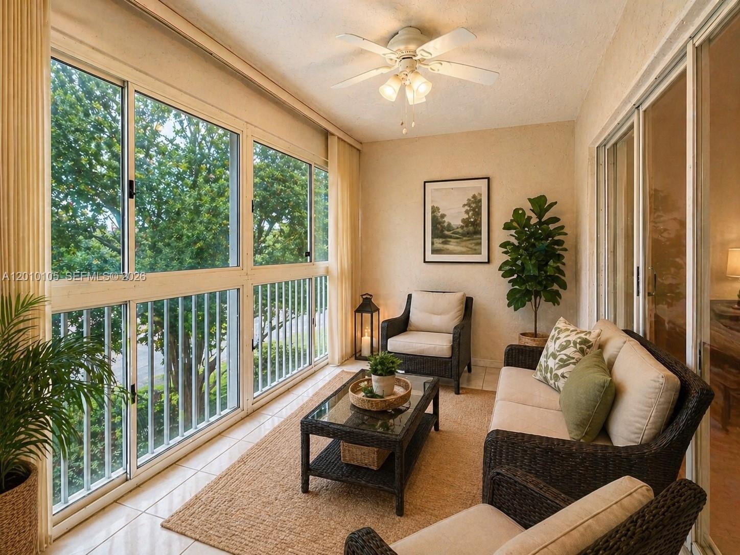 A sunroom with wicker furniture, a glass-top coffee table, and large windows overlooking trees — 5016 Rose Hill Dr # 2303, Boynton Beach FL 33437, BOYNTON BEACH, FL