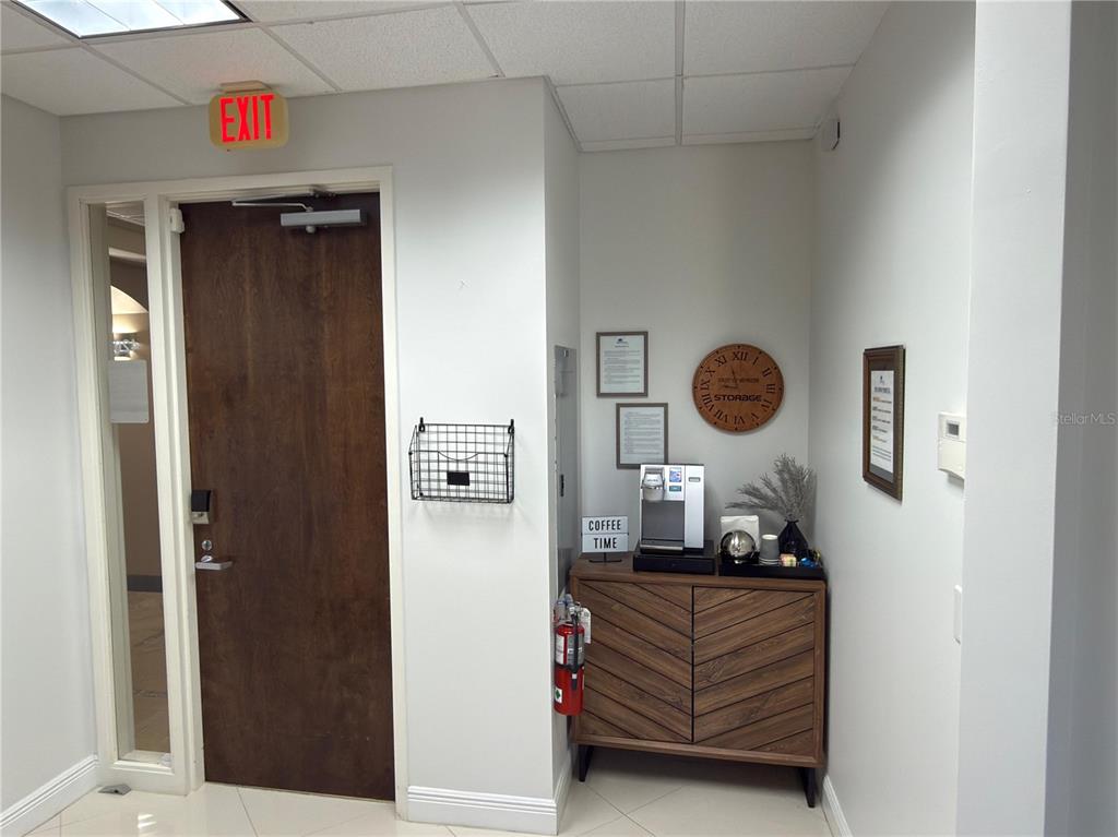 An office corner features a wooden coffee station, a wall clock, and an exit door — 6735 CONROY ROAD UNIT 420, ORLANDO, FL