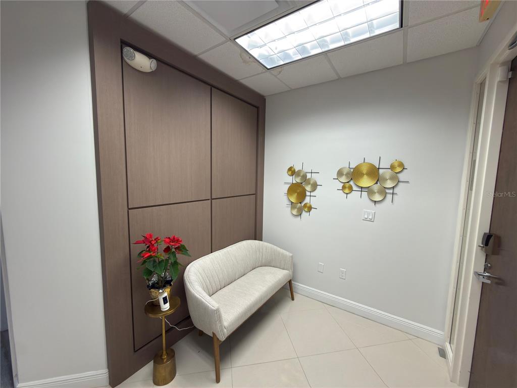 A small waiting area features a light-colored settee, gold wall art, and a wood-paneled wall — 6735 CONROY ROAD UNIT 420, ORLANDO, FL