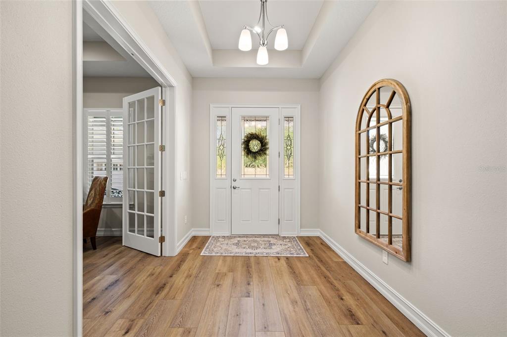 A bright entryway features wood-look flooring, a tray ceiling with a chandelier, and a mirror — 4829 HICKORY OAK DRIVE, BROOKSVILLE, FL