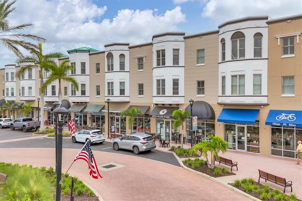 An exterior view of a multi-story commercial building with storefronts and a brick-paved plaza — 8111 LAKEWOOD MAIN STREET UNIT 306, LAKEWOOD RANCH, FL