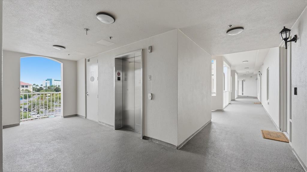 An outdoor apartment building hallway features a metal elevator, white walls, and a balcony view — 8111 LAKEWOOD MAIN STREET UNIT 306, LAKEWOOD RANCH, FL