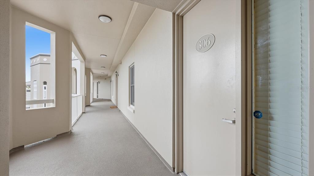 An outdoor apartment hallway features a beige door labeled 306 and a view of buildings — 8111 LAKEWOOD MAIN STREET UNIT 306, LAKEWOOD RANCH, FL