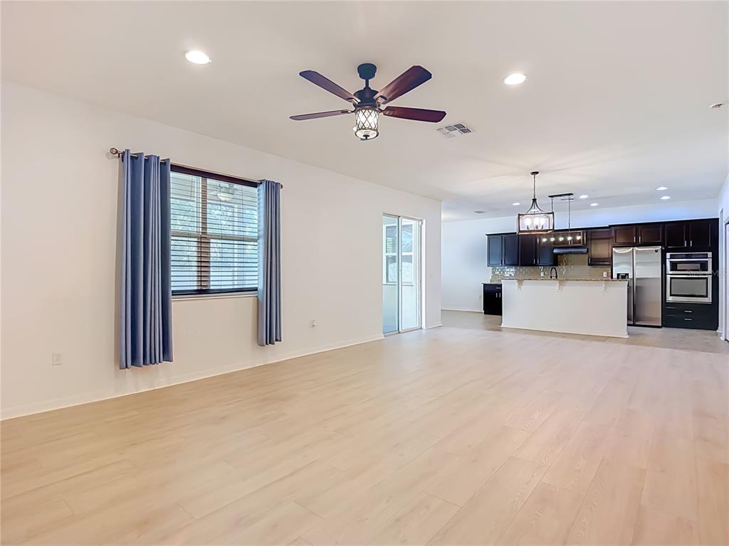 An open-concept living room with light wood flooring leads to a kitchen with dark cabinetry — 1113 CANYON OAKS DRIVE, BRANDON, FL
