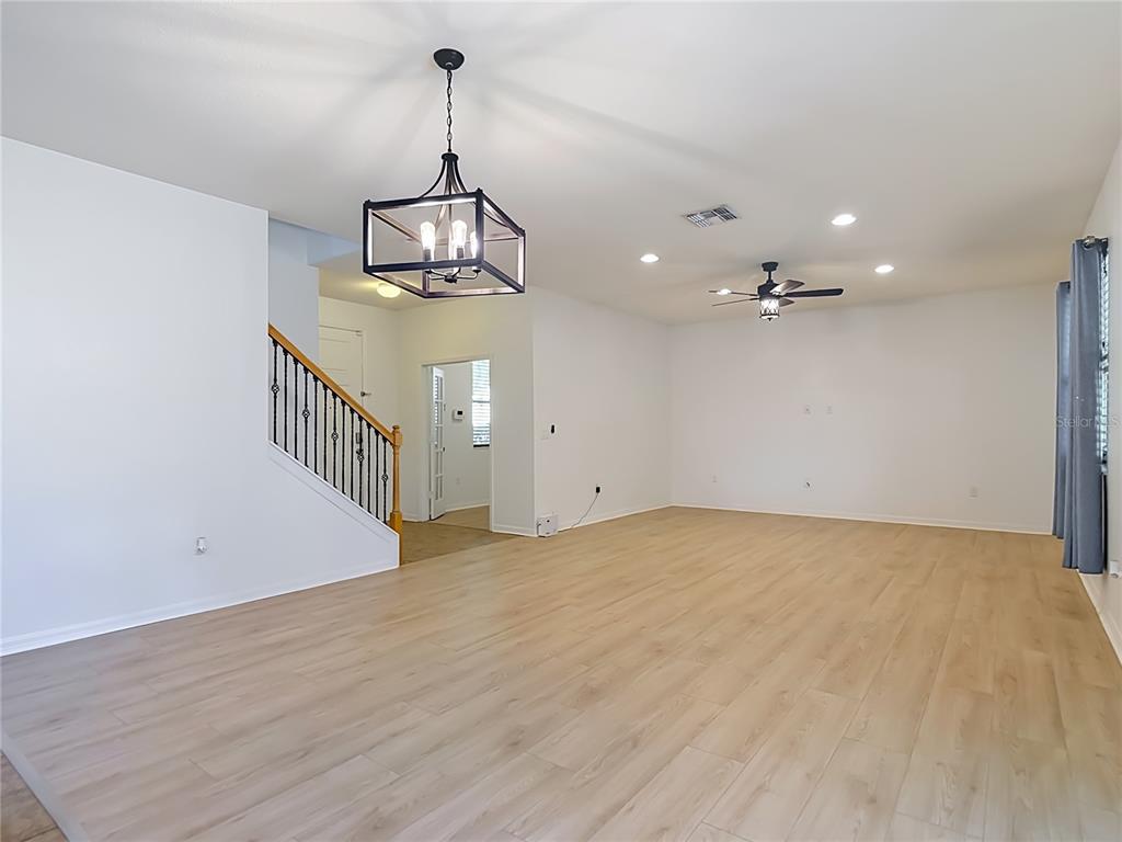 An open-plan living area features light wood-look flooring, a staircase with iron railings, and lighting — 1113 CANYON OAKS DRIVE, BRANDON, FL