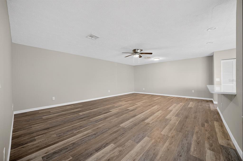 A spacious, empty living room with light gray walls, wood-look flooring, and a ceiling fan — 2948 TANGERINE COURT, LEESBURG, FL