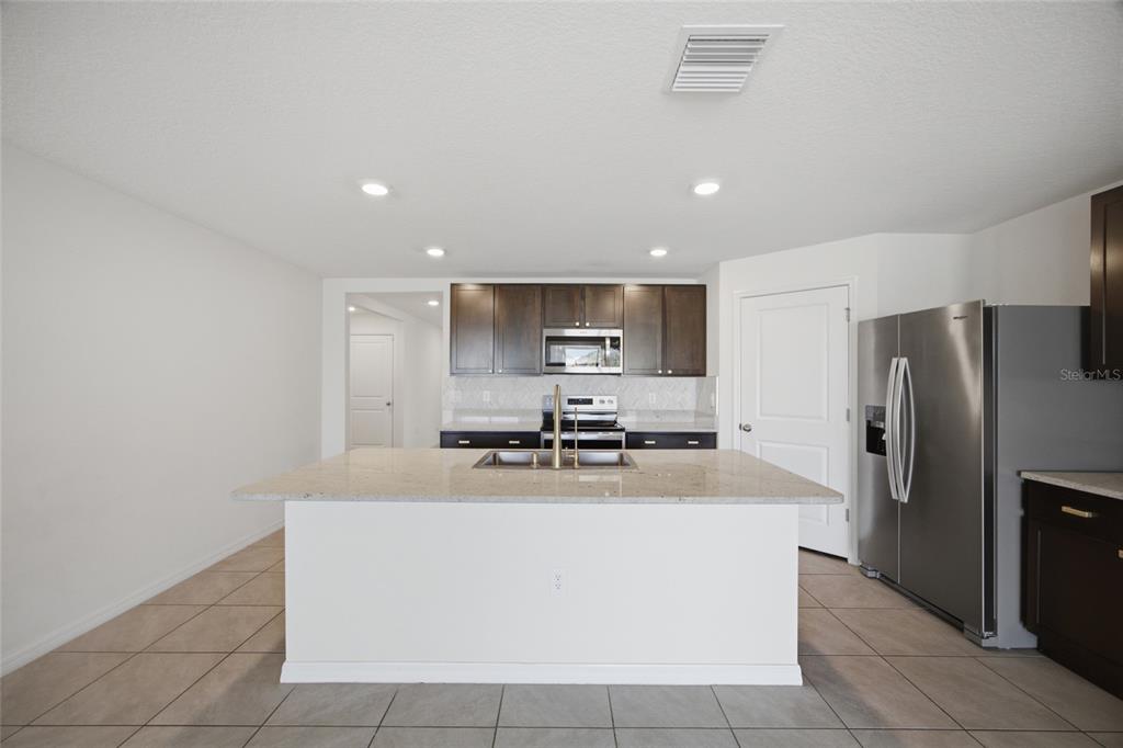 A kitchen features a white island with a sink, dark cabinets, and stainless steel appliances — 2812 GUMBO LIMBO DRIVE, WIMAUMA, FL