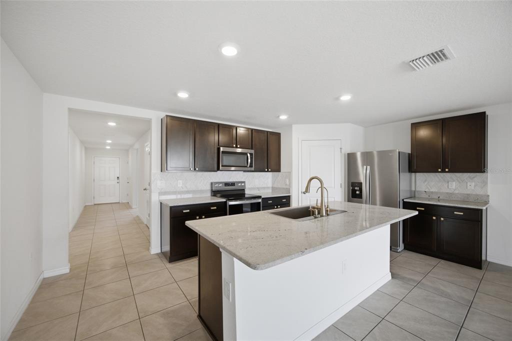 A kitchen features dark wood cabinets, granite countertops, a center island, and stainless steel appliances — 2812 GUMBO LIMBO DRIVE, WIMAUMA, FL
