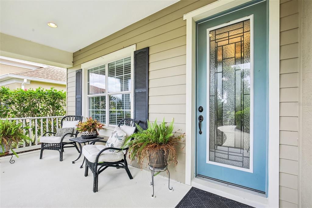 A covered front porch features two wicker chairs, a small table, and a blue door — 12307 WHISPER LAKE DRIVE, BRADENTON, FL
